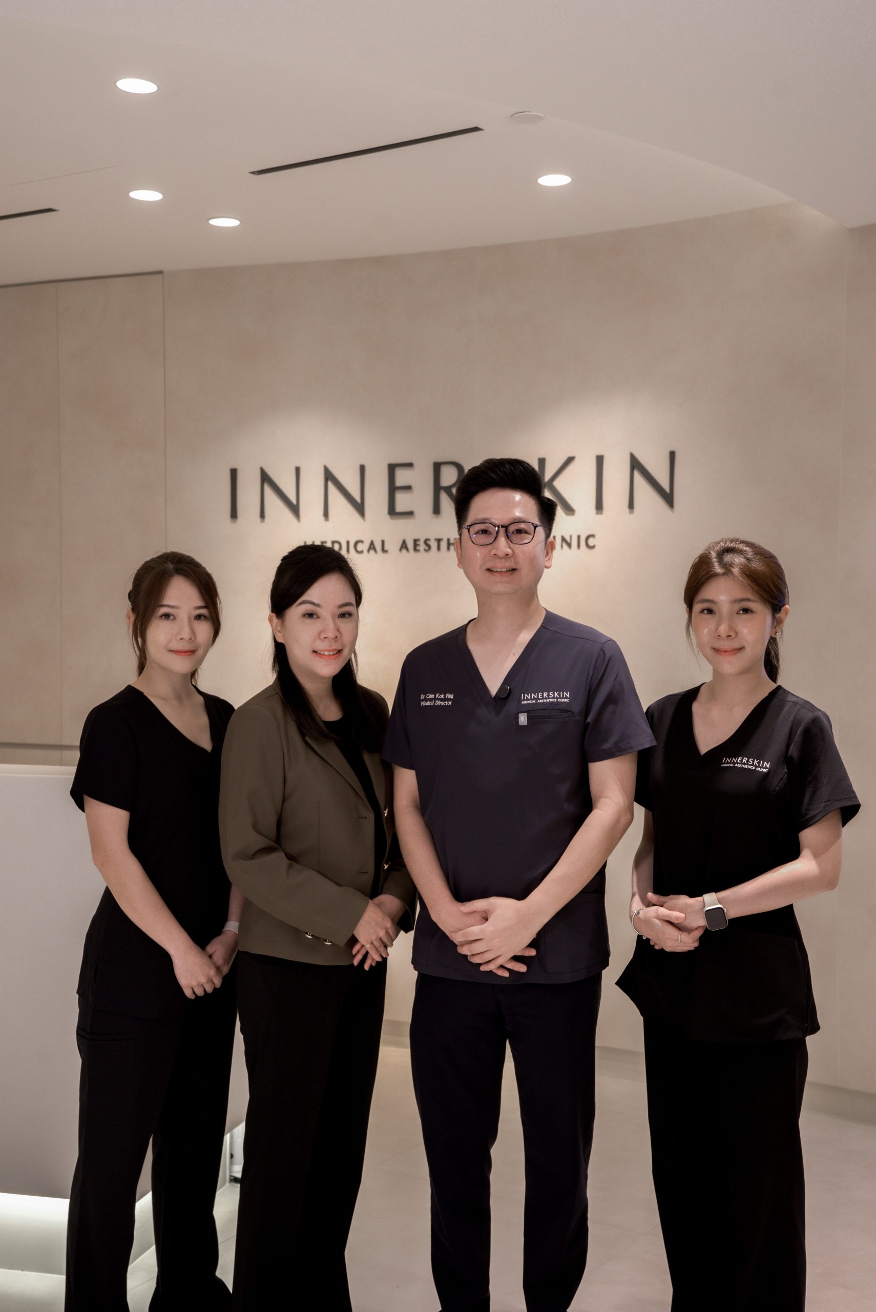 Innerskin doctor and clinic team standing in front of the reception logo wall